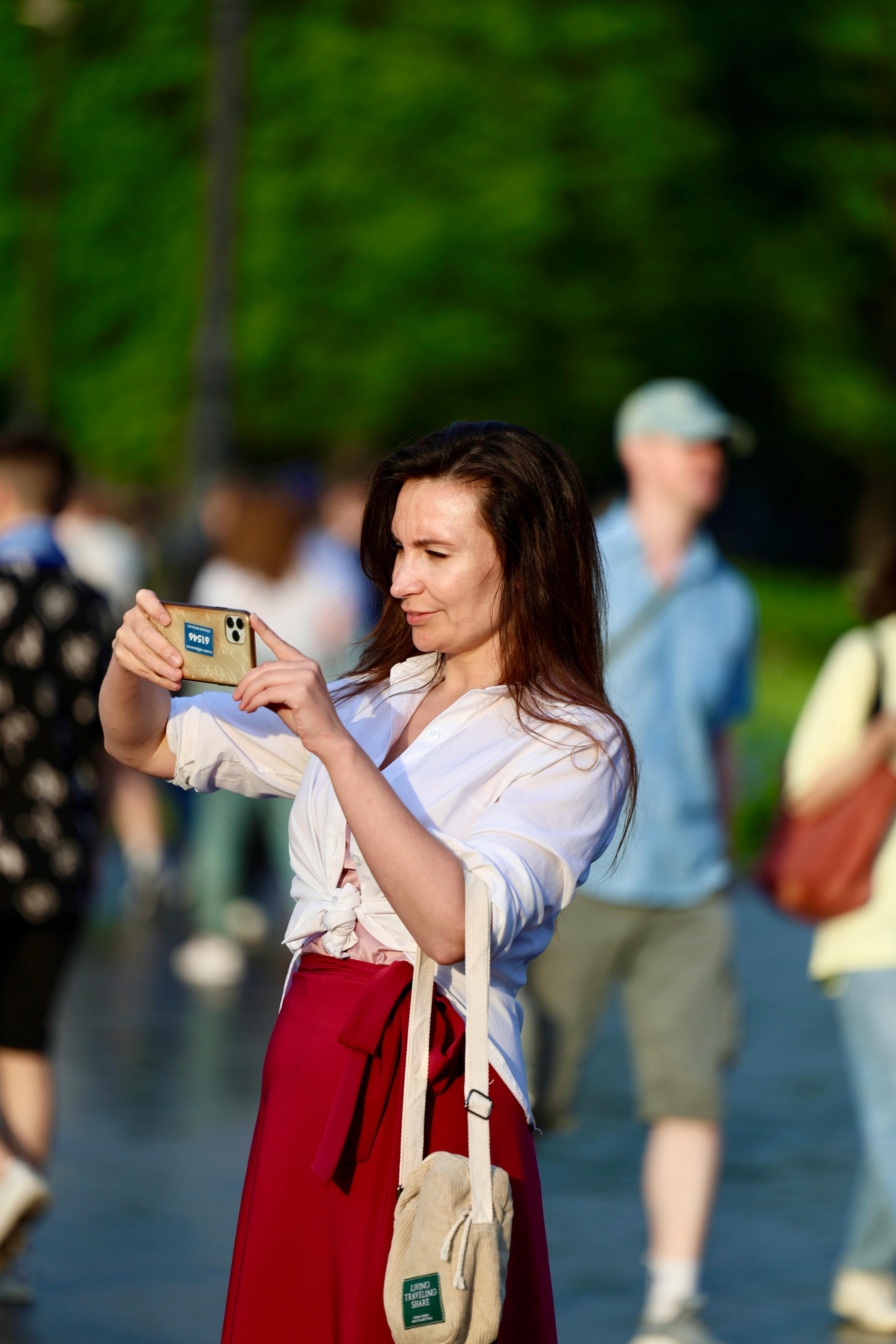 Free Woman taking a photo with smartphone in a busy urban setting during summer. Stock Photo