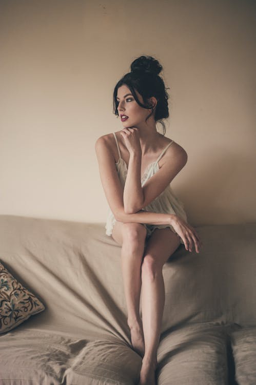 美麗的女人，穿著白色的晚禮服，坐在沙發的靠背上，看著別處的照片