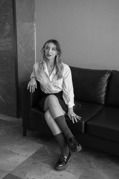 A fashionable young woman in a white blouse seated on a black sofa, exuding elegance.