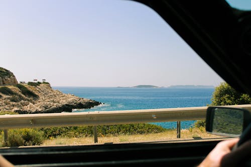 A person driving a car with the ocean in the background