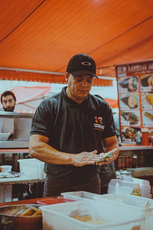 A man in black shirt and black hat at a food stand