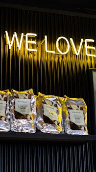 Colorful coffee bags under a glowing neon 'WE LOVE' sign on a black shelf.