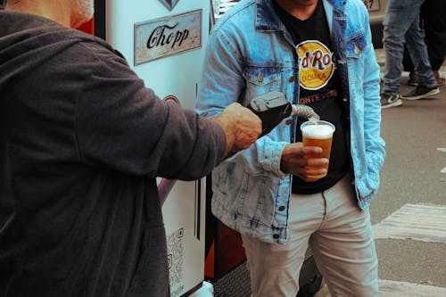 A man is holding a beer and another man is holding a bottle of soda