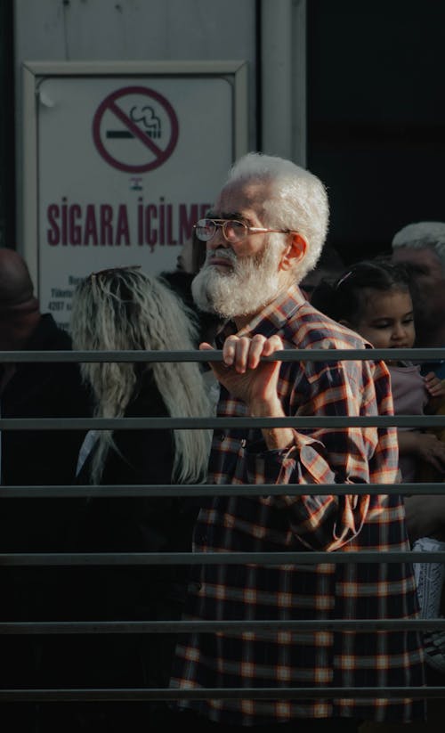 A man with a beard and glasses standing in front of a fence