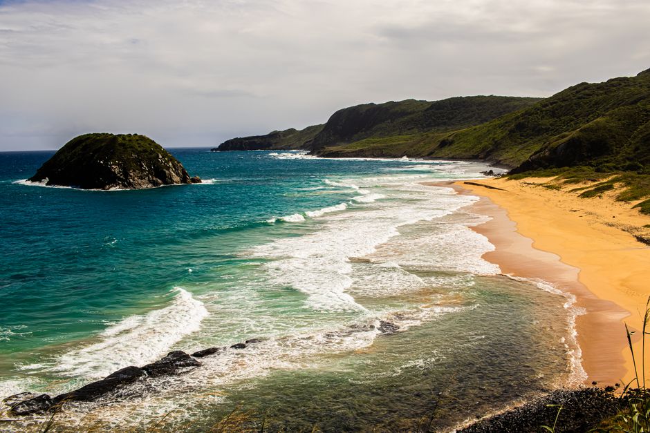 Breathtaking view of a coastal landscape featuring turquoise waters, sandy beach, and lush green cliffs.
