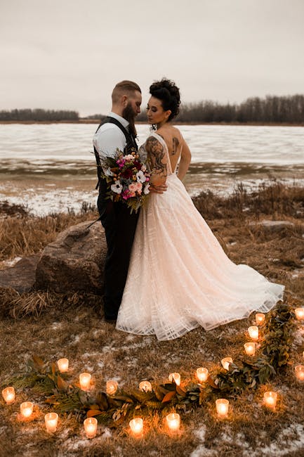 A couple embraces in a warm, rustic outdoor wedding setting by a frozen lake.