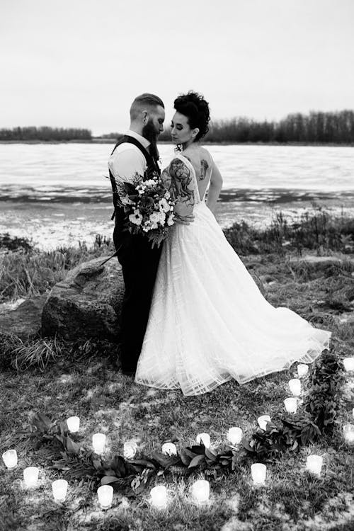 男人和女人穿着婚纱站在灰色的照片中的柱子蜡烛包围的水体附近
