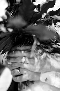 Close-up of bride and groom's hands with rings and bouquet in monochrome.