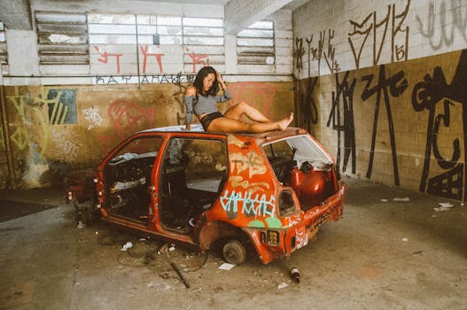A woman sitting on an abandoned car in a graffiti-covered urban setting.