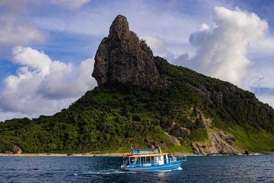A vibrant boat sails by a stunning rocky island with lush greenery under a dramatic sky.