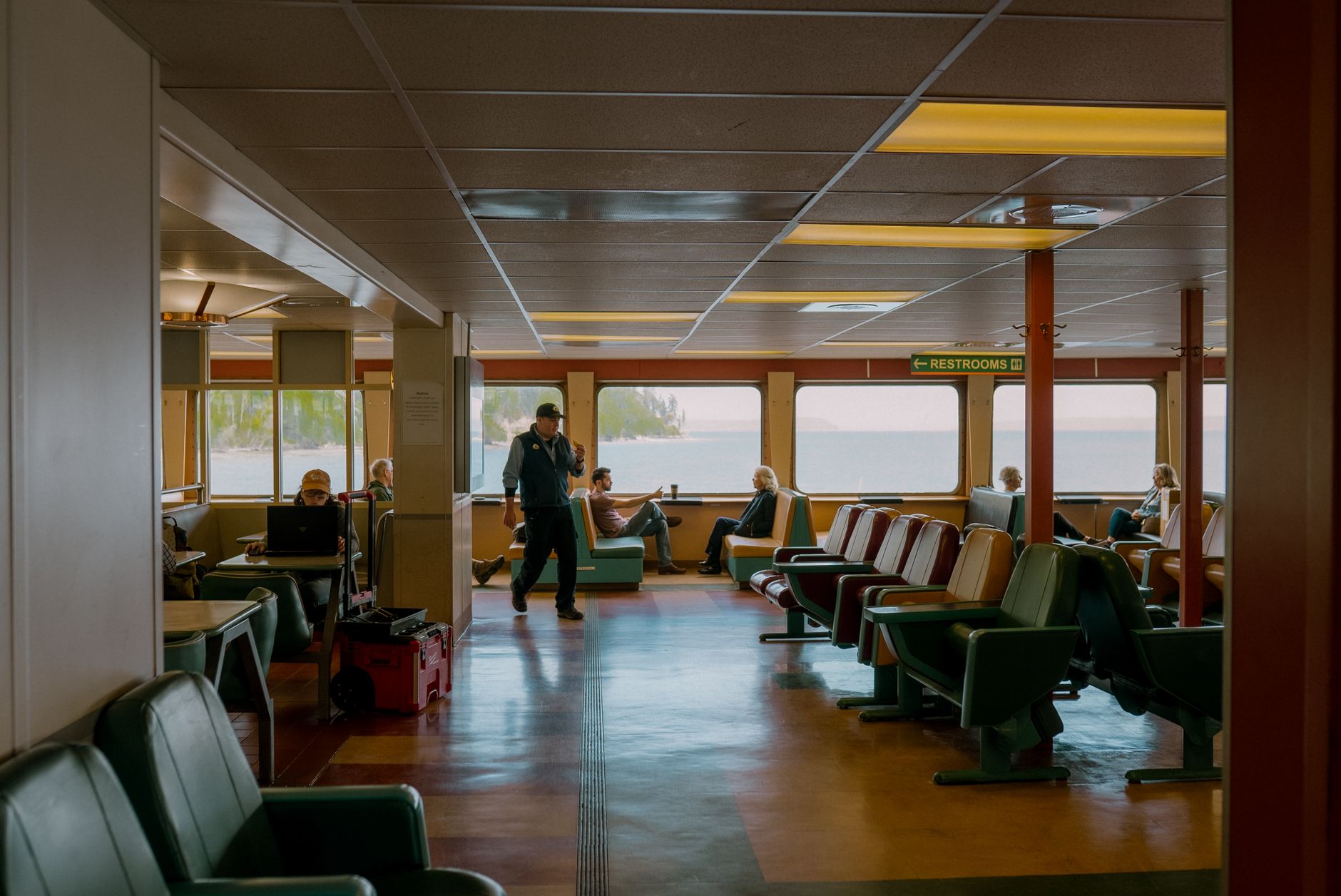 Relaxed passengers on a Seattle ferry with scenic water views. Interior seating and restrooms in view.