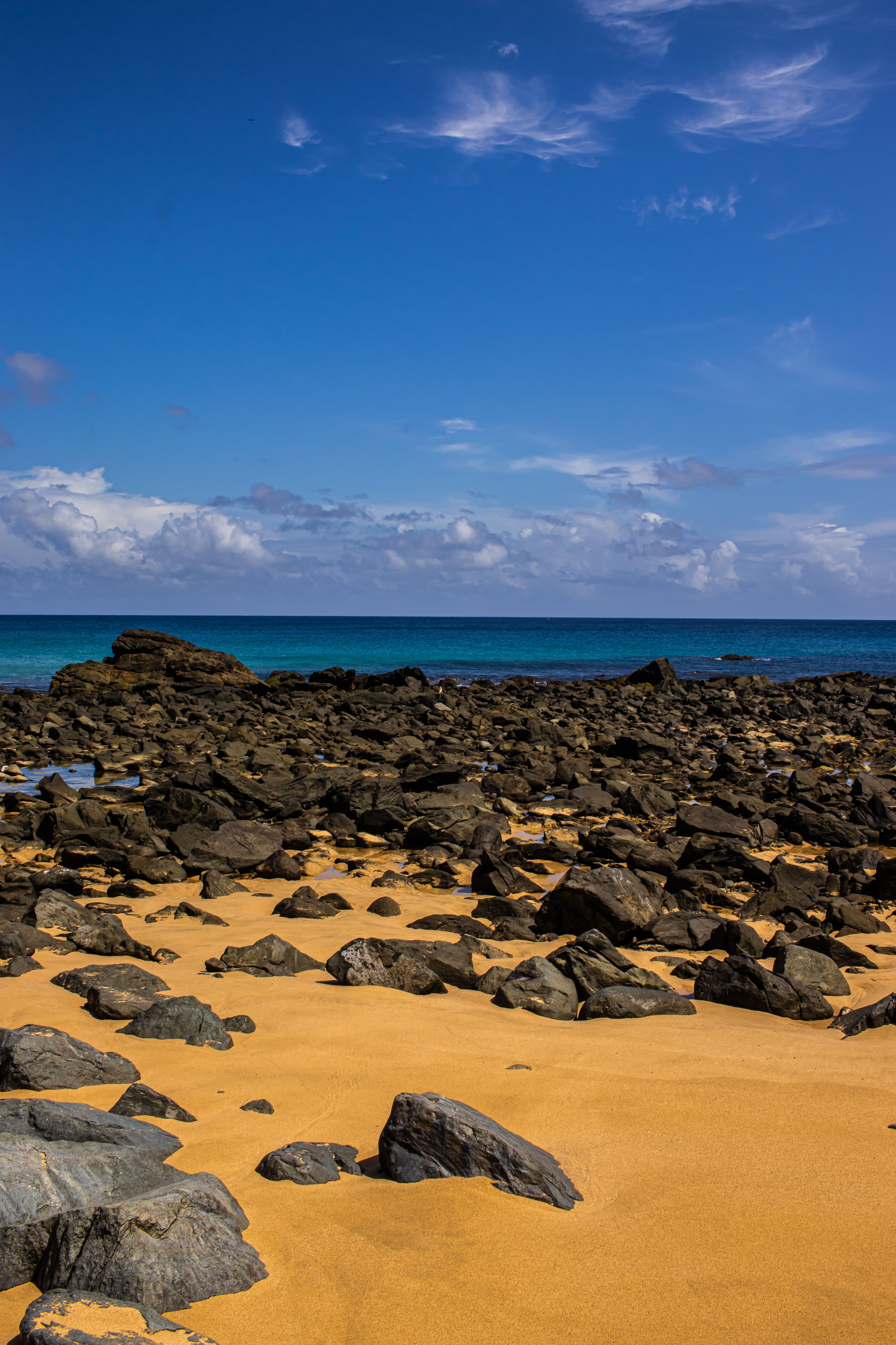 A sandy beach with rocks and blue sky · Free Stock Photo