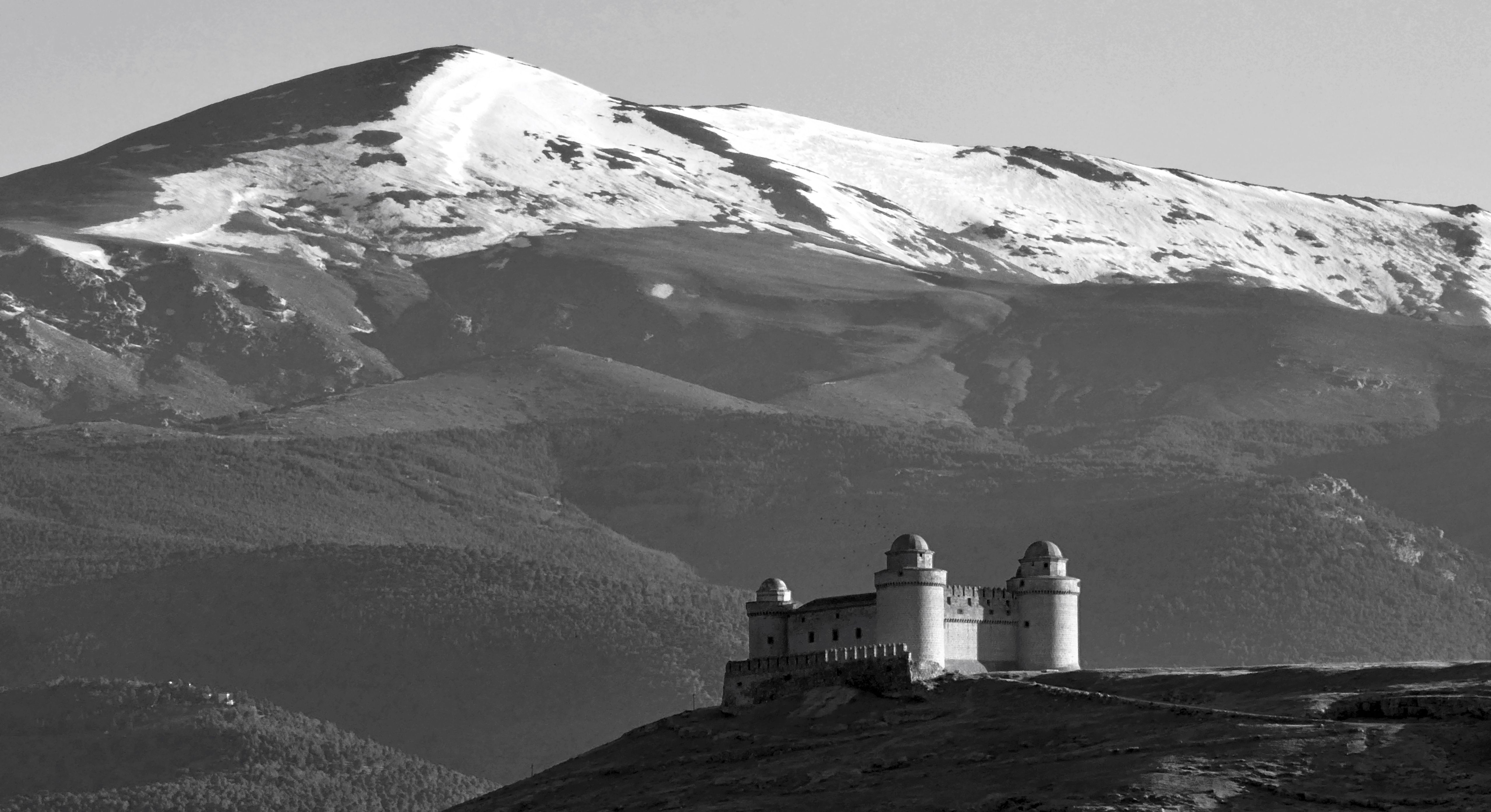Black and white view of Castillo de La Calahorra set before snowcapped mountains in Spain.