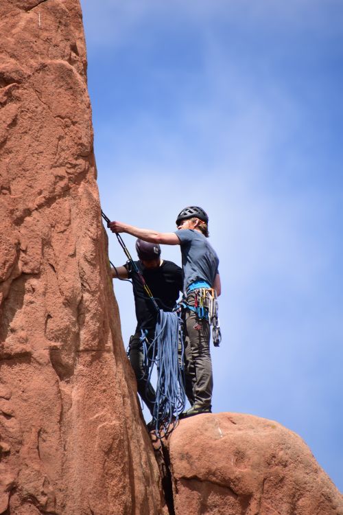 Free Two climbers with helmets and gear ascending a red sandstone cliff under a clear blue sky. Stock Photo
