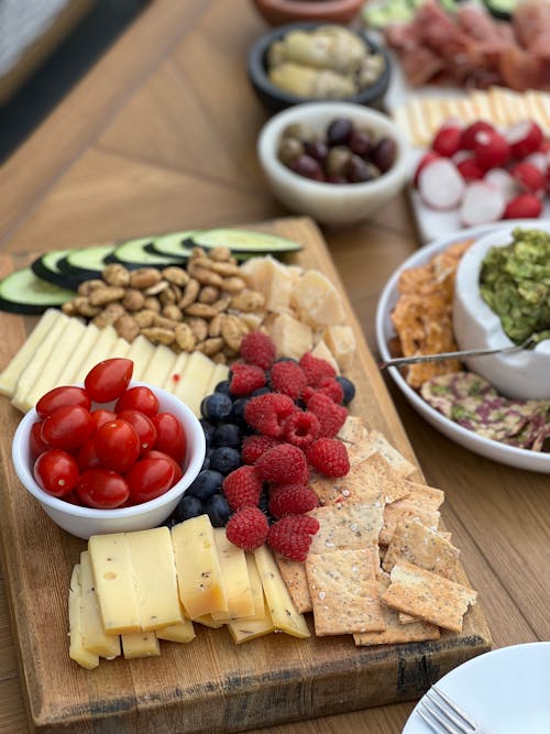 A wooden cutting board with cheese, crackers, fruit and nuts