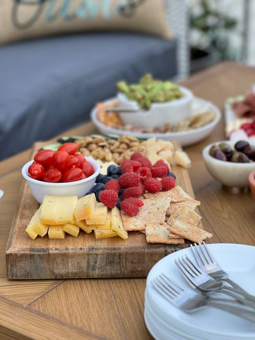 A wooden cutting board with fruit, nuts and crackers