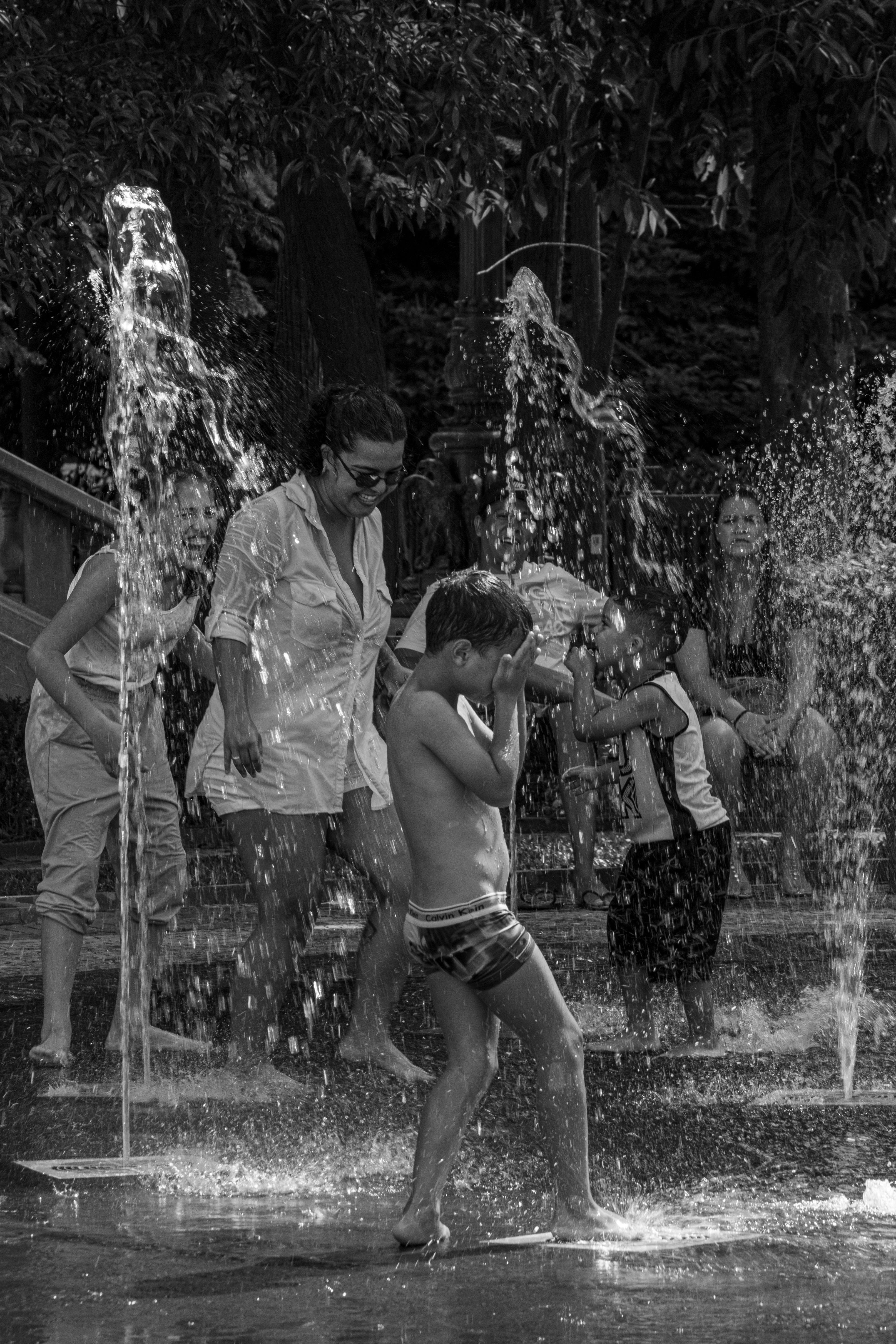 Black and white image of children playing in a water fountain on a hot summer day.