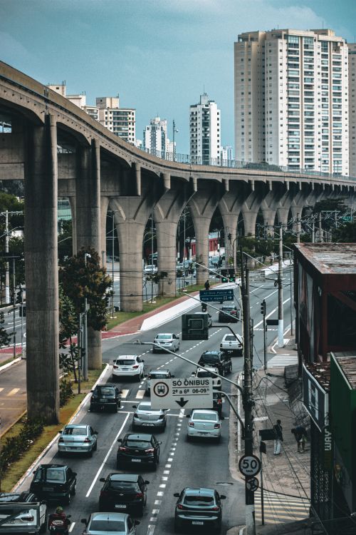 Free A bustling urban highway with traffic beneath an elevated rail and towering buildings in the background. Stock Photo