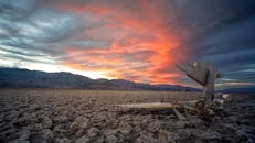 贫瘠的沙漠地形上，一架废弃的飞机残骸置于前景，被引人注目的日落照亮