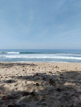 A serene beach scene with waves gently crashing on the shore under a clear blue sky.