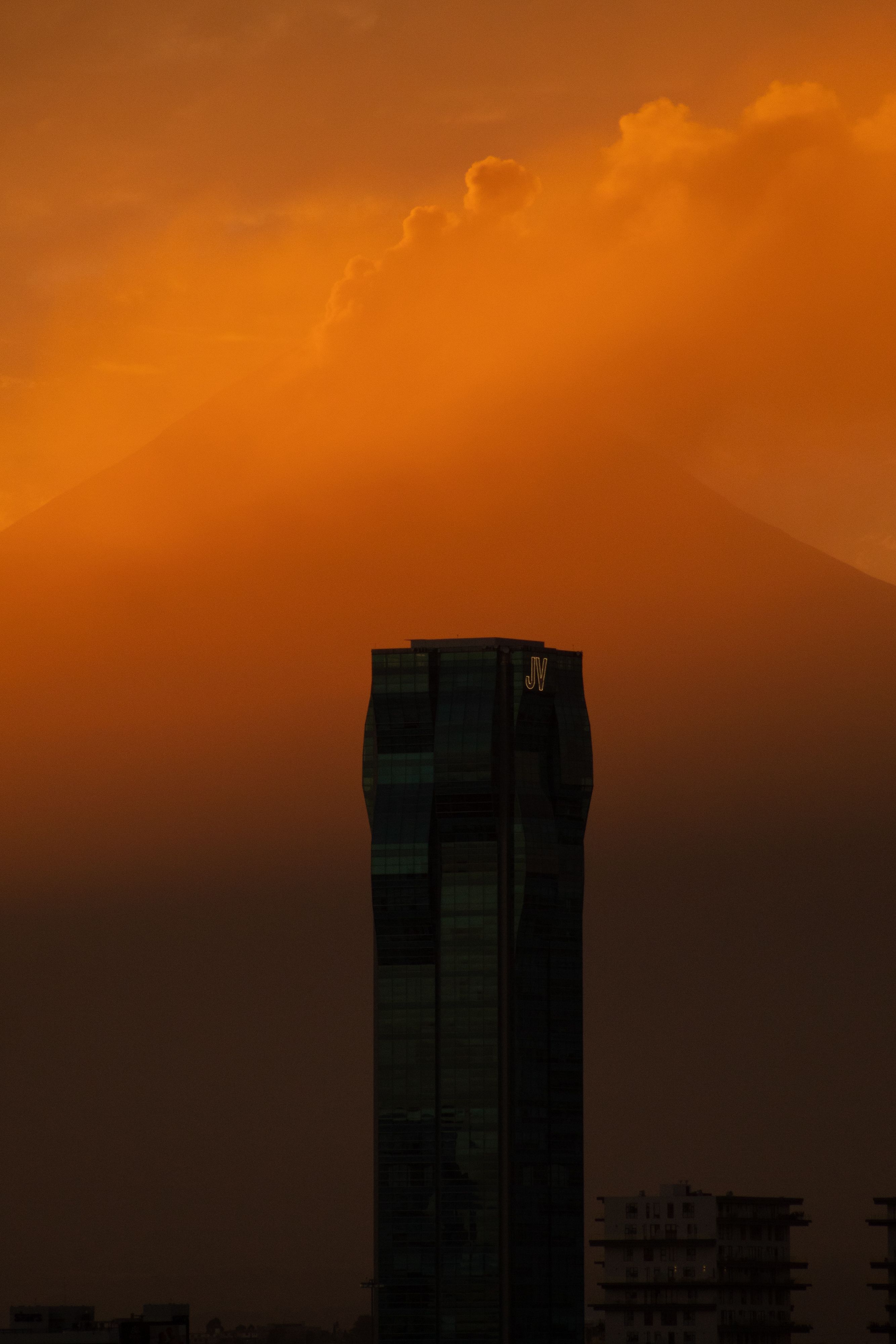 A dramatic sunset casts vibrant hues over a striking modern skyscraper in Puebla, Mexico.