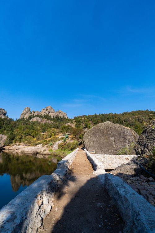 Free Discover a serene stone pathway in Pachuca, surrounded by lush greenery and rocky landscapes under a clear blue sky. Stock Photo