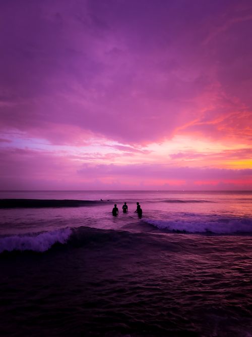 Free Captivating view of the ocean at sunset with silhouetted figures in the water under vibrant skies. Stock Photo