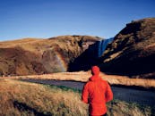  A person admiring a rainbow that’s appearing beside a waterfall in Iceland