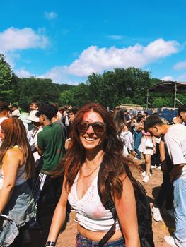 Smiling woman at a vibrant outdoor festival with colored powders and joyful crowd.