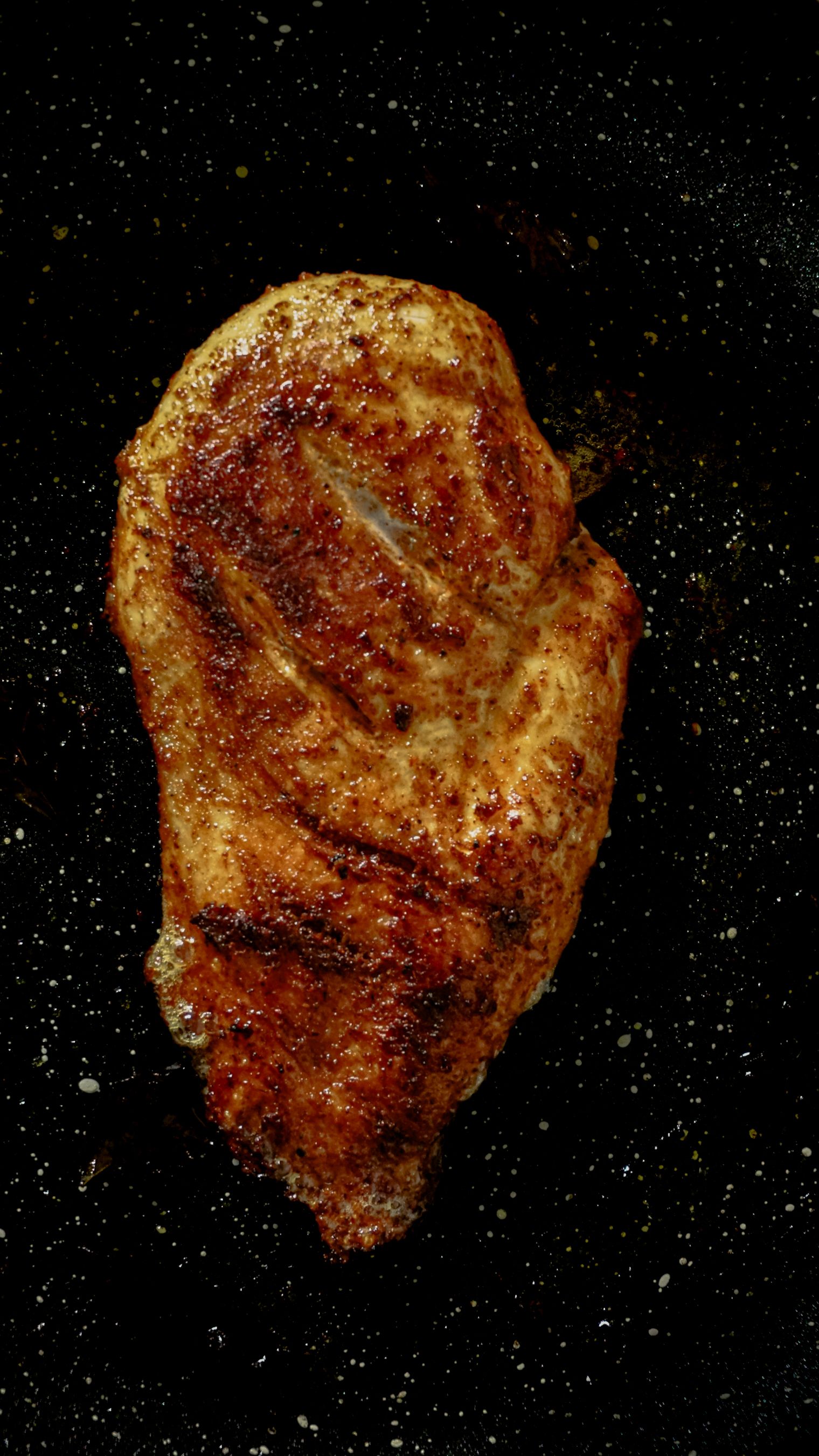 Juicy grilled chicken breast on a black speckled surface, top view.