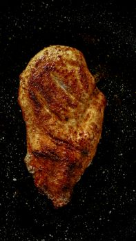 Juicy grilled chicken breast on a black speckled surface, top view.