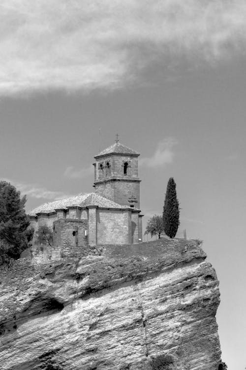 A black and white photo of a church on top of a cliff