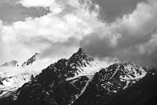 Black and white photo of snow-covered mountains in Almaty, Kazakhstan, under dramatic clouds.