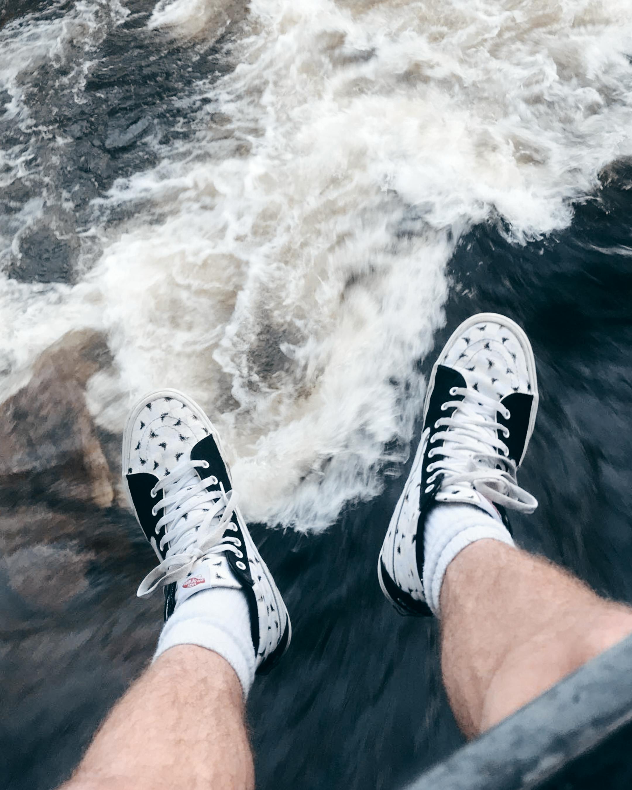 在科罗拉多州博尔德市的一条河上，一双悬挂的腿展示着时尚的运动鞋，背景是流动的河水