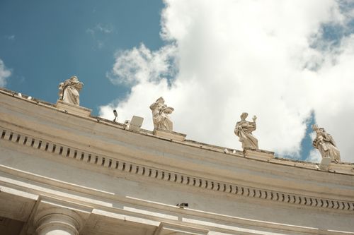 Free Low angle view of sculptures atop a Vatican City building against a blue sky and clouds. Stock Photo