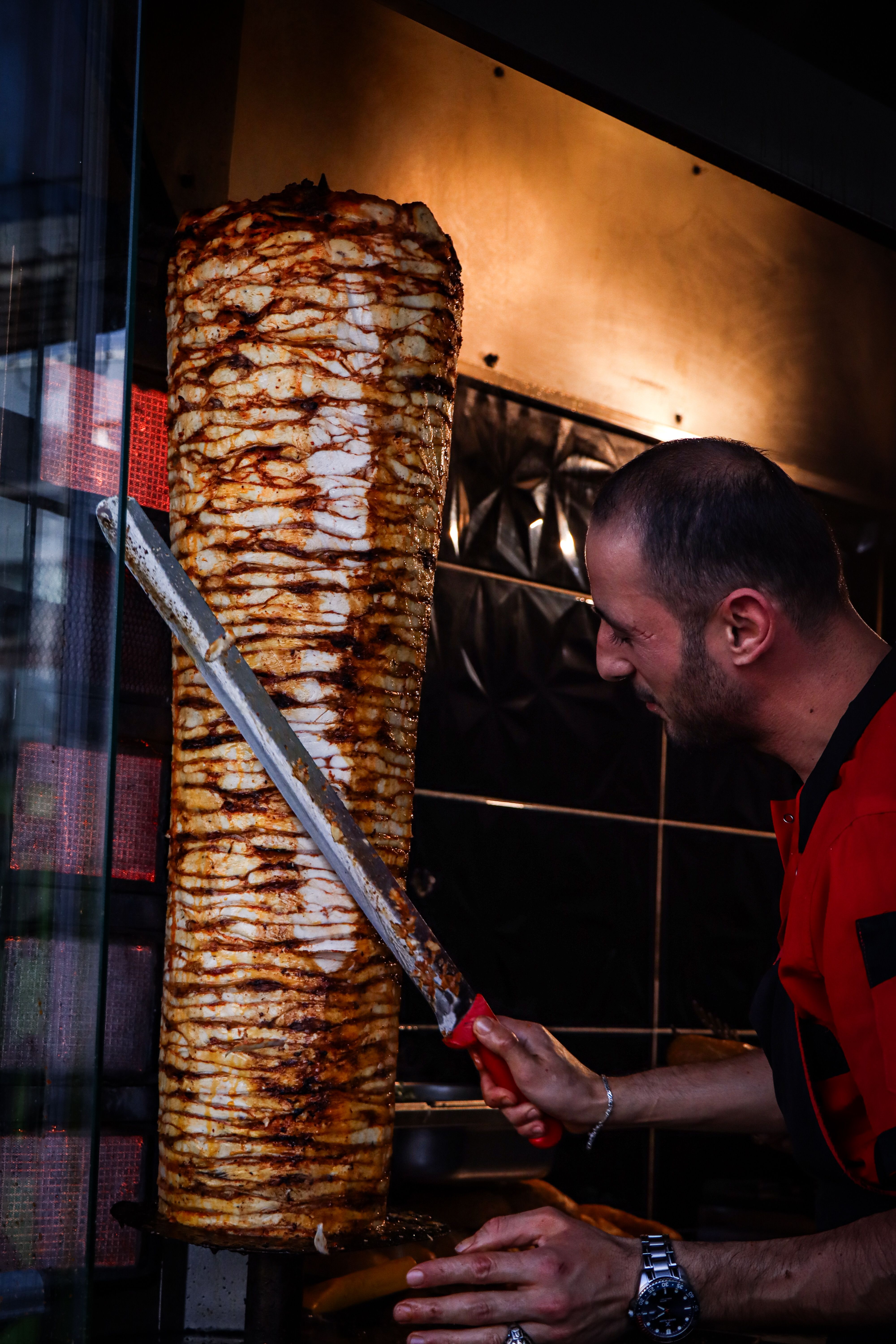 Longue lame appuyée contre la broche verticale de viande empilée, cuisinier de profil dans la pénombre