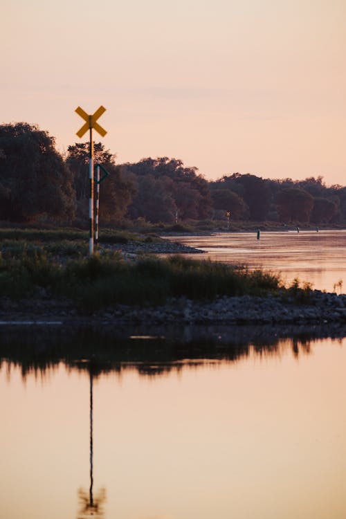 A railroad crossing sign is on the side of a river