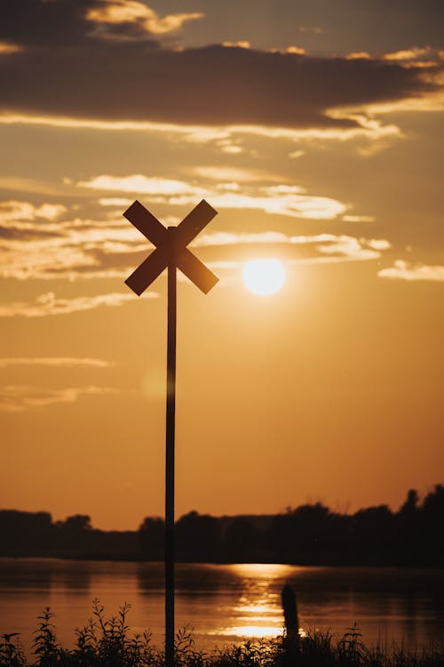 A railroad crossing sign is silhouetted against the sunset