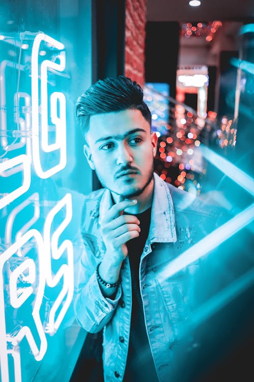 Man Wearing Denim Jacket Beside Neon Lighted Signage