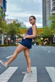 Fashionable woman posing casually on an urban crosswalk in a vibrant city street.