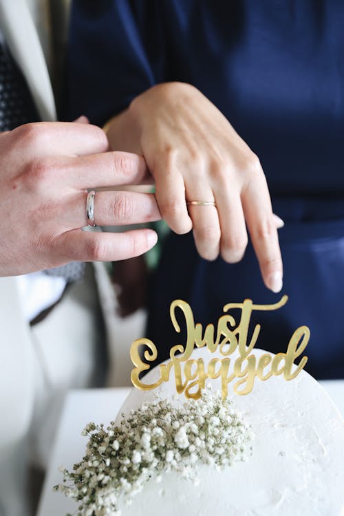 Close-up of a Couple Holding Their Hands above a Cake with a Sign Saying "Just Engaged"