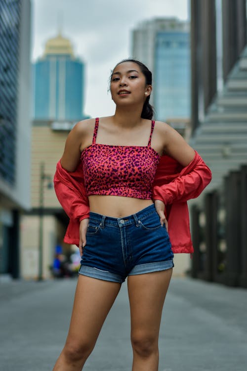 Selective Focus Photography of Woman in Red Jacket and Blue Denim Short Holding Her Waist