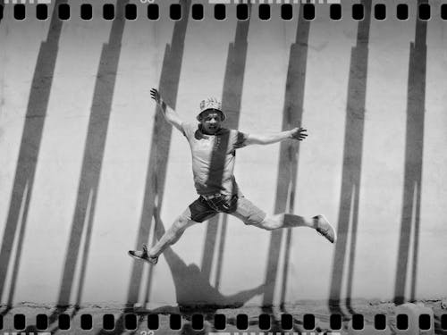 Grayscale Photo of Jumping Man Beside Concrete Wall