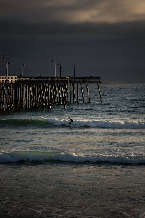 A surfer rides a wave at the pier