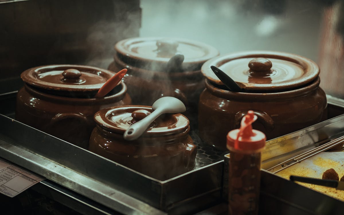 Close-up of steaming traditional clay pots with utensils on a stove, creating a cozy kitchen ambiance.