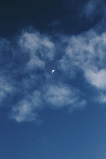 A serene night sky with the moon peeking through scattered clouds in Rio Vermelho, Brazil.