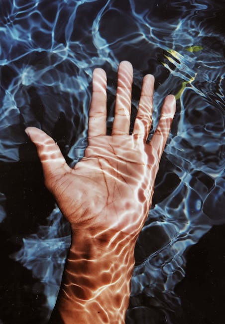 A hand submerged in clear blue water with captivating ripple effects, creating a soothing and artistic look.