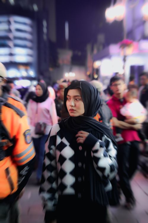 Free A young woman wearing a headscarf walks through a bustling urban street at night. Stock Photo