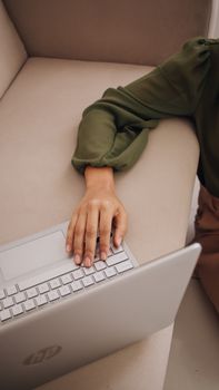 Woman in a green shirt working on a laptop while sitting on a comfortable beige sofa.