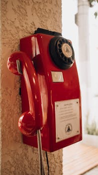 A red vintage rotary dial telephone mounted on a textured wall indoors.